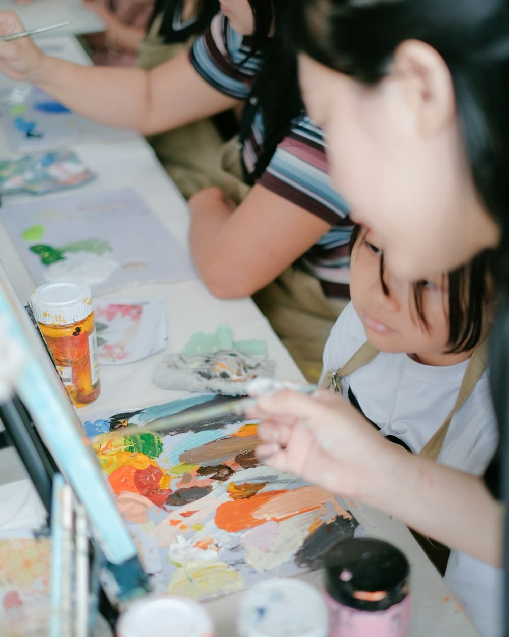 Niña de edad escolar pintando con acuarelas en la mesa de talleres